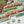 A close-up of a completed jigsaw puzzle showing a colorful landscape scene with layered tan and green hills, water, and foliage. Three loose puzzle pieces are placed on a white surface below the puzzle.