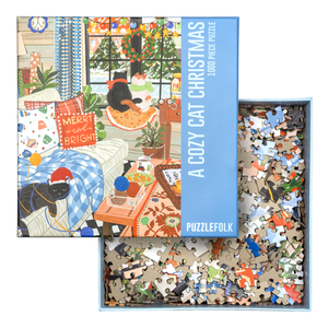Open puzzle box with pieces visible in the bottom with lid resting on top. Lid is blue with an image of several cats enjoying a holiday decorated room. 
