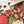 A close-up of a completed jigsaw puzzle showing a colorful holiday design with red ornaments, green leaves, orange flowers, and white snowflakes, with a few loose puzzle pieces on a light surface.