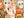 A hand holds several small, random cut puzzle pieces with an autumn and Halloween-theme, set against a festive, out-of-focus shot of a partial view of the completed jigsaw puzzle.