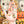 A hand holds several small, random cut puzzle pieces with an autumn and Halloween-theme, set against a festive, out-of-focus shot of a partial view of the completed jigsaw puzzle.