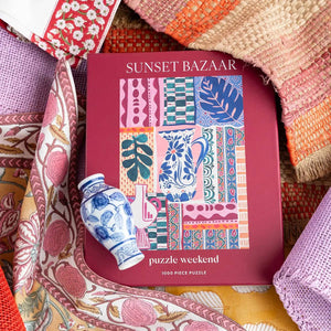 Puzzle box titled 'Sunset Bazaar' shown with a decorative vase on a colorful fabric background