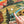 A close-up of a completed landscape jigsaw puzzle showing a colorful mountain valley scene with trees, a river, bison, and a corner of the rainbow layers of a hot spring. A person's finger pushes a piece towards a empty section of the puzzle. 