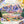 Almost complete puzzle showing lovely valley and mountain scene on white table surrounded by flowers, puzzle box and puzzle poster. 