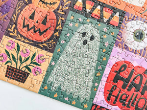 Partial view of a completed Halloween-themed jigsaw puzzle centered on the artwork of a floral designed ghost on muted green background with stars, also visible are a pumpkin, candy corn, eyeball and living flowers with sharp teeth. 