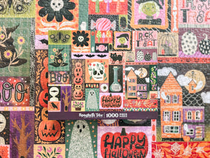A 1000-piece jigsaw puzzle box titled by Spaghetti Tree puzzles featuring a colorful collage of Halloween-themed illustrations like pumpkins, ghosts, houses, and 'Happy Halloween' signs, set atop an out of focus shot of the completed puzzle.