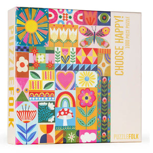 A colorful jigsaw puzzle box from PuzzleFolk featuring a vibrant patchwork design with flowers, butterflies, rainbows, and geometric patterns. The box is white on the right side with yellow text reading 'CHOOSE HAPPY! 1000 PIECE PUZZLE' and 'PUZZLEFOLK' at the bottom.