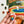 A hand holds a random-cut jigsaw puzzle piece with a rainbow pattern in front of a partially completed colorful puzzle.