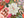 A hand holds a small, colorful jigsaw puzzle piece featuring a pink and white floral design, set against a background of a jigsaw puzzle with a winter holiday theme.