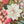 A hand holds a small, colorful jigsaw puzzle piece featuring a pink and white floral design, set against a background of a jigsaw puzzle with a winter holiday theme.