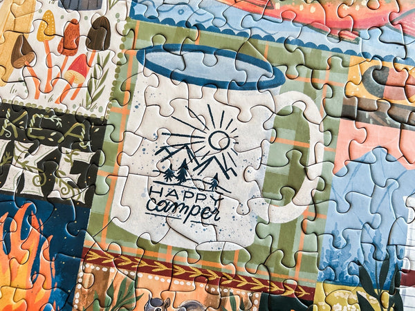 Jigsaw puzzle with 'Happy Camper' design and various outdoor-themed pieces.
