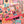 A 500-piece jigsaw puzzle box by Spaghetti Trees featuring a colorful autumn patchwork design with pumpkins, corn, leaves, and plaid patterns, displayed on a out of focus shot of a completed version of that puzzle in the background.