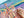 A close-up of a colorful jigsaw puzzle showing an abstract landscape or canyon scene, with a hand holding a small pink puzzle piece over the blank white gap in the puzzle.