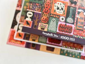 A close-up of a Spaghetti Tree 1000-piece Halloween jigsaw puzzle box, showing colorful illustrated panels with pumpkins, a skull, ghost, house, and 'Happy Halloween' text, photographed on a light background and out of focus completed puzzle and print of the artwork.